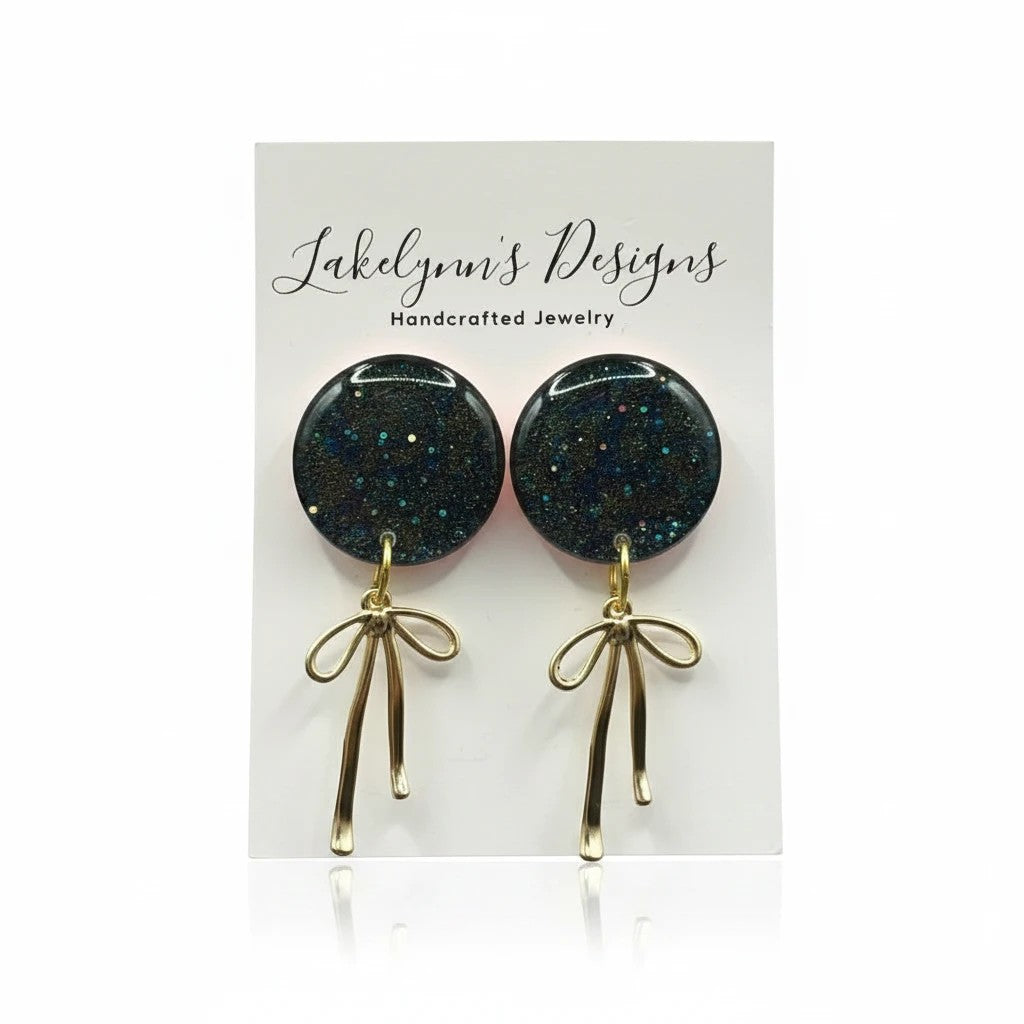 Lakelynns Designs round glitter earrings with gold-tone bow dangle. Dark blue glitter studs with iridescent flecks.
