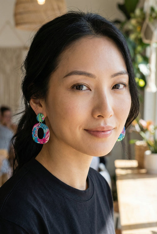 Lakelynns Designs oval hoop earrings with colorful floral pattern in blue, pink, and green, suspended from circular studs.