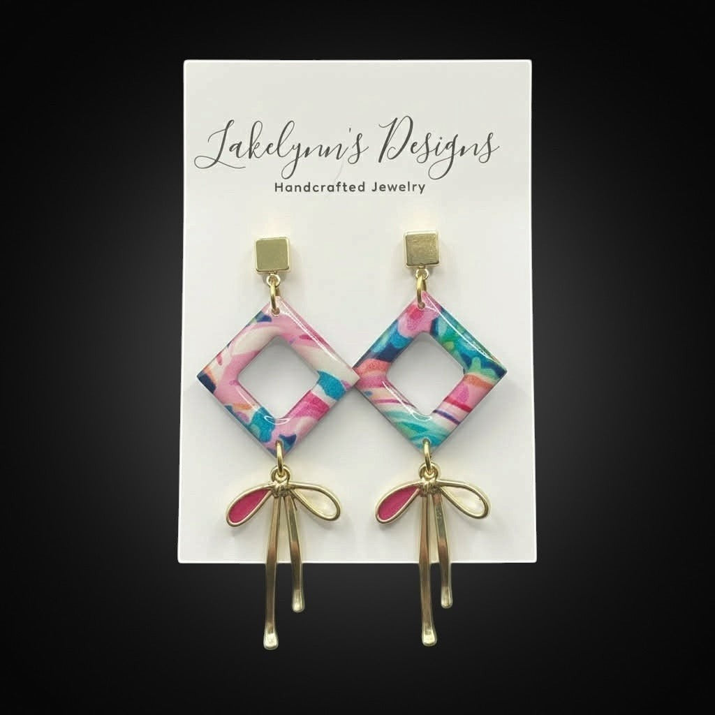 Lakelynns Designs abstract diamond dangle earrings with pink, blue, teal, and white pattern and gold bow accents.