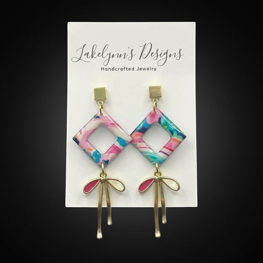 Lakelynns Designs abstract diamond dangle earrings with pink, blue, teal, and white pattern and gold bow accents.