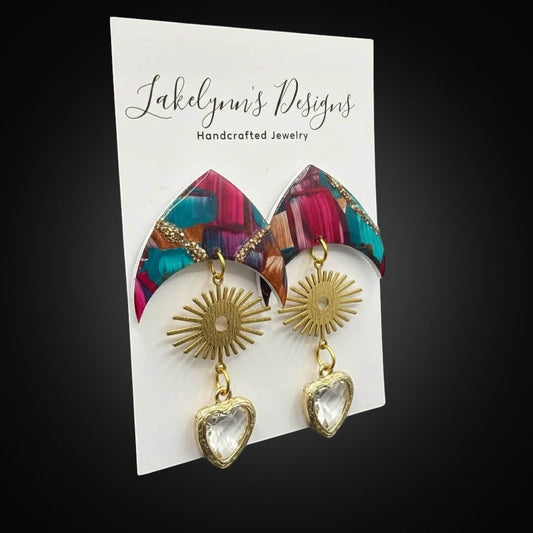 Lakelynns Designs abstract heart dangle earrings with gold sunburst charms and clear faceted heart pendants in pink, blue, and earth tones.