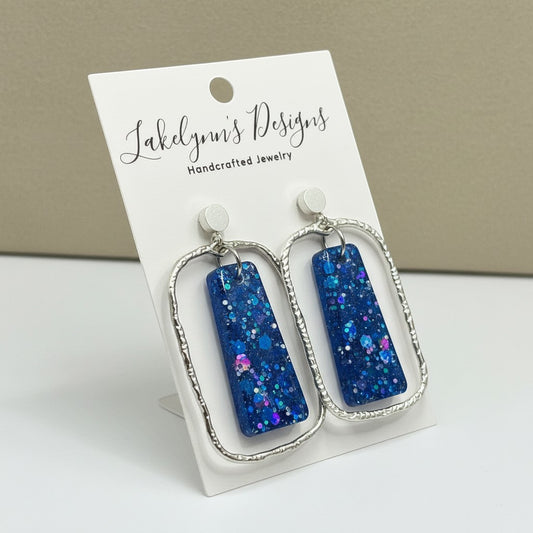 Lakelynns Designs rectangular blue glitter resin dangle earrings with textured silver-tone frames.