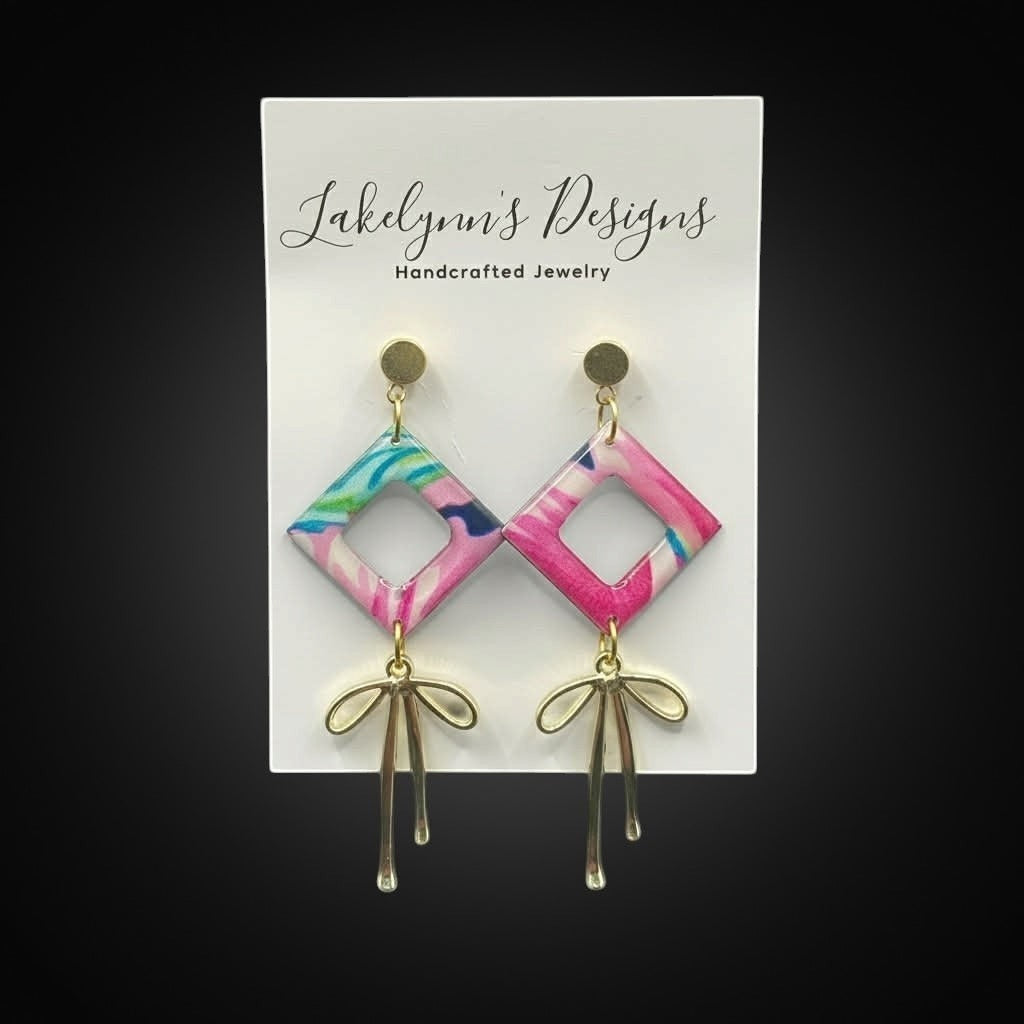 Lakelynns Designs Camila dangle earrings with pink, blue, and green abstract pattern and gold bow accent.