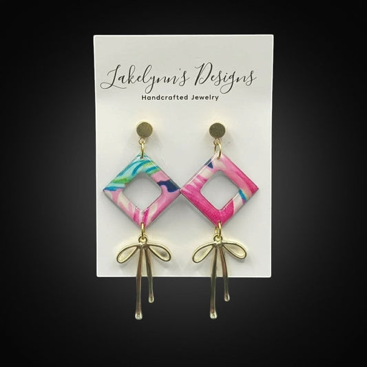 Lakelynns Designs Camila dangle earrings with pink, blue, and green abstract pattern and gold bow accent.