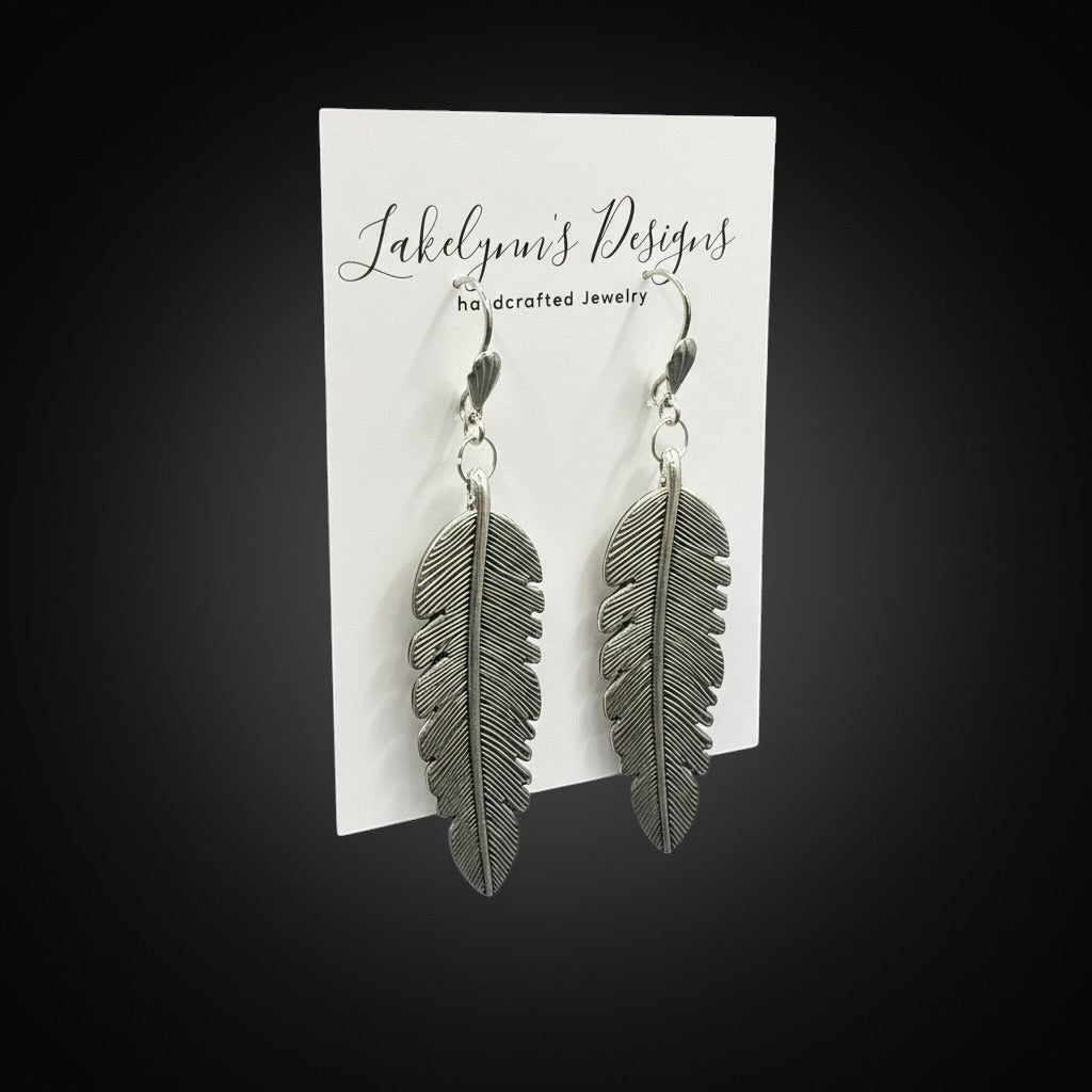 Lakelynns Designs Maren Feather Drop Earrings, silver-tone metal with intricate feather design, dangling from hooks.