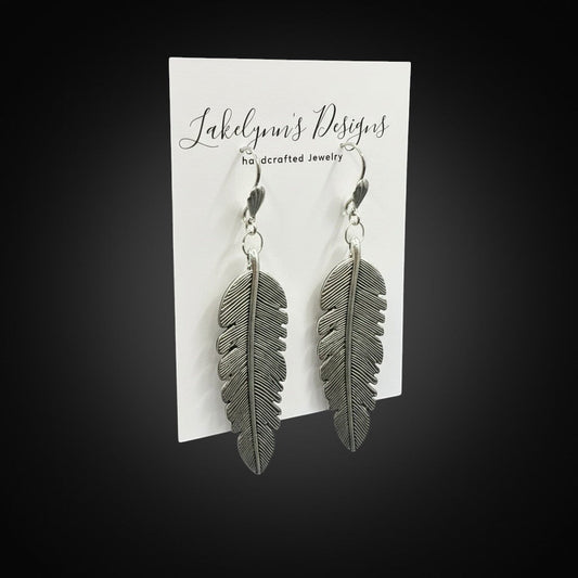 Lakelynns Designs Maren Feather Drop Earrings, silver-tone metal with intricate feather design, dangling from hooks.