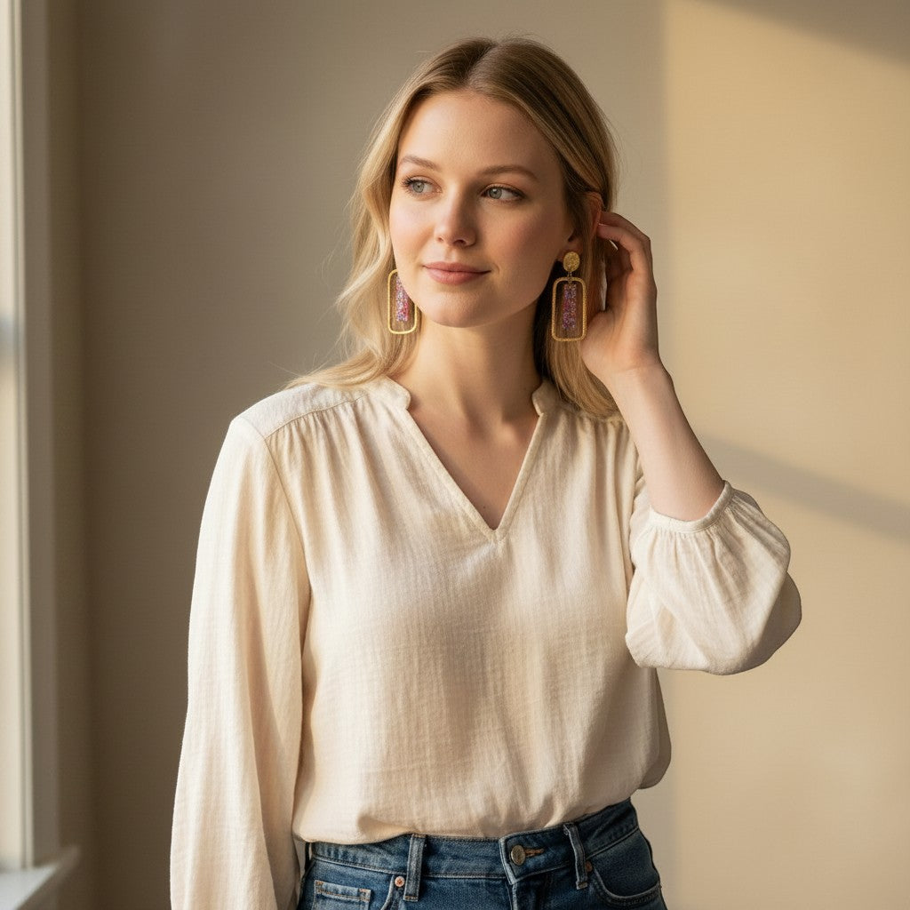 Lakelynns Designs Gemma gold rectangular earrings with purple beaded inlay on a blonde model wearing a cream blouse.