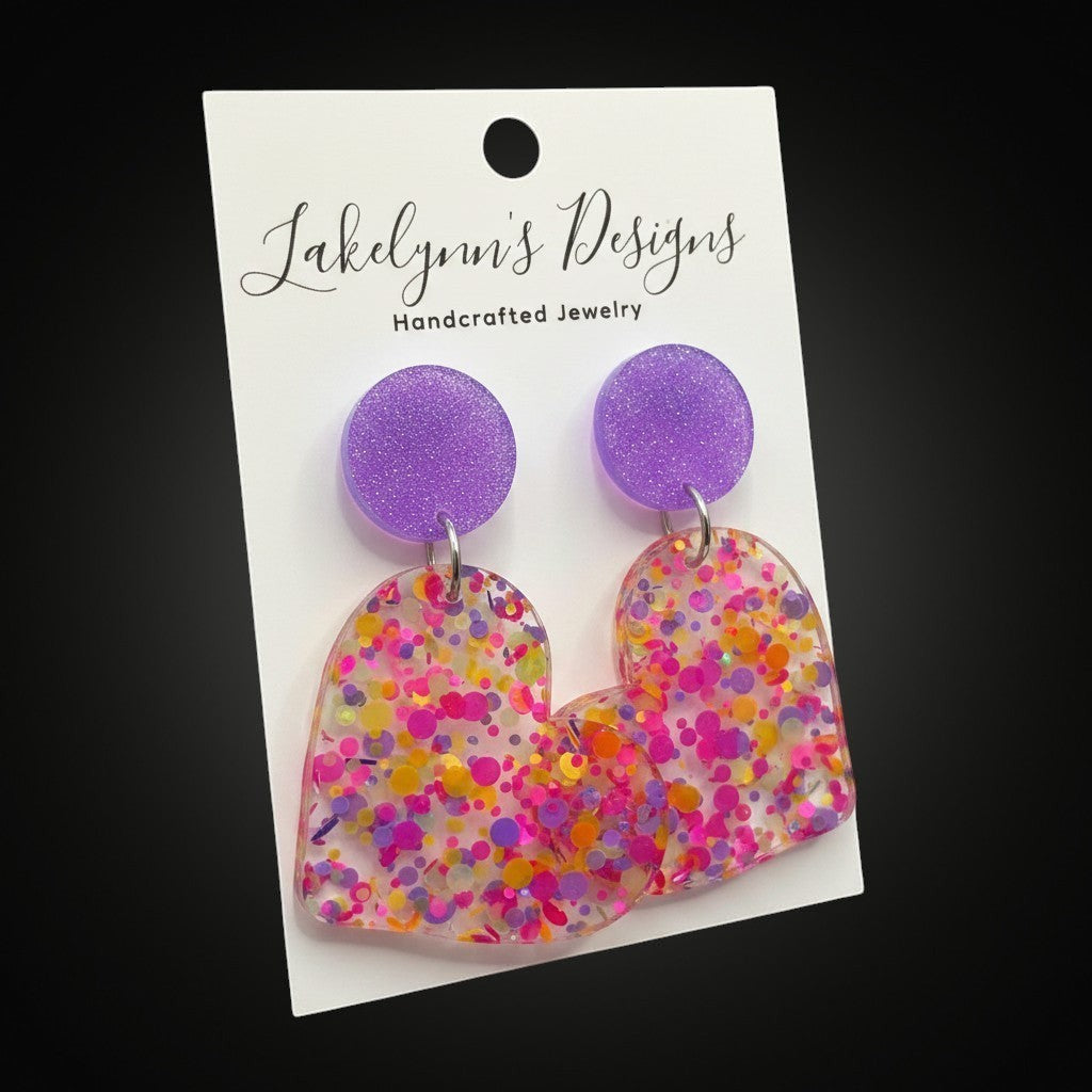 Lakelynns Designs multi-colored glitter heart dangle earrings with purple stud backs. Clear acrylic with pink, yellow, and orange glitter.