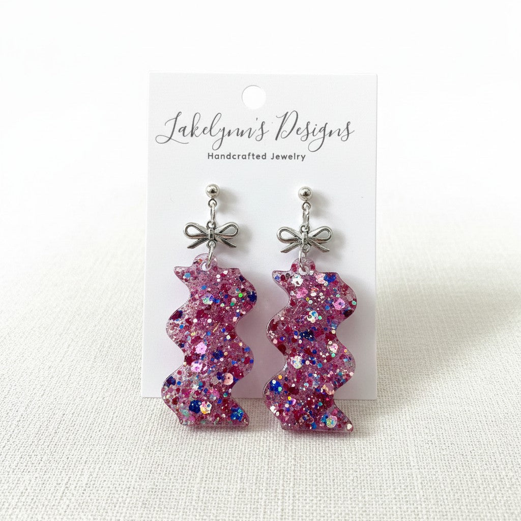 Lakelynns Designs pink, purple, and blue glittery zigzag resin earrings with silver-tone bow accents.