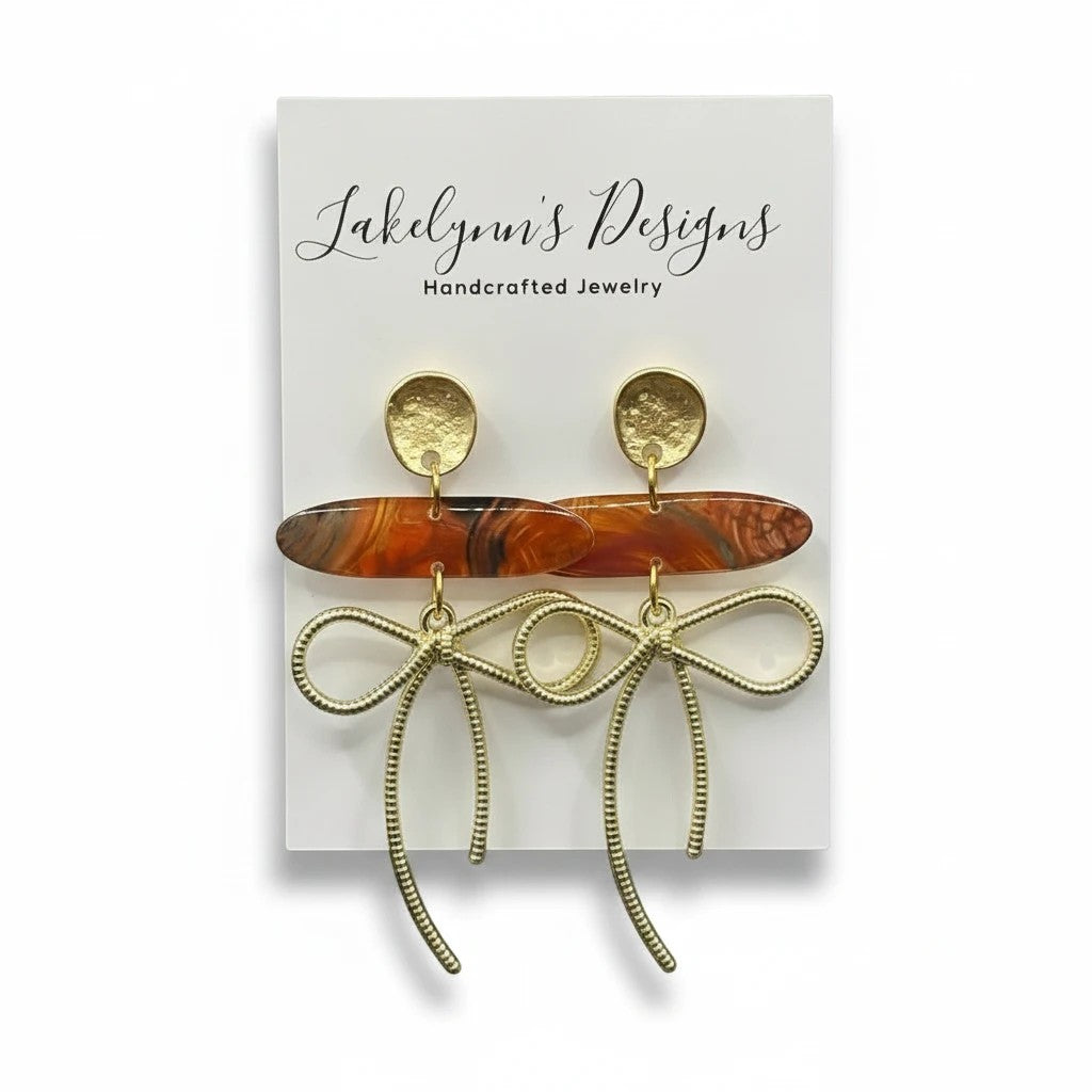 Lakelynns Designs gold bow dangle earrings with marbled oval acrylic bead in warm earth tones.