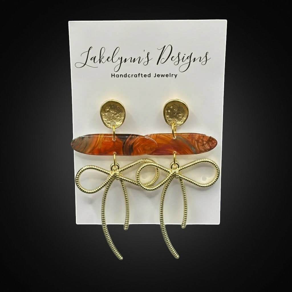 Lakelynns Designs gold bow dangle earrings with marbled orange acrylic bead and textured gold stud.