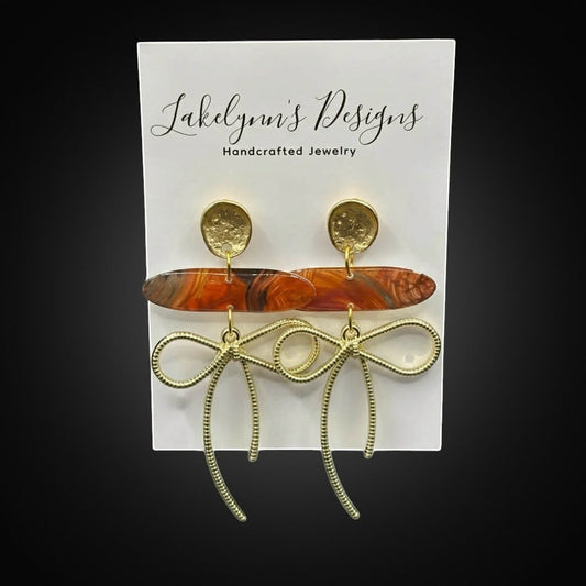 Lakelynns Designs gold bow dangle earrings with marbled orange acrylic bead and textured gold stud.