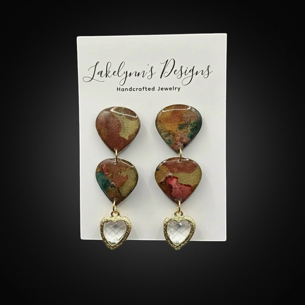 Lakelynns Designs marbled rust, gold, and green heart-shaped dangle earrings with clear faceted heart charms.