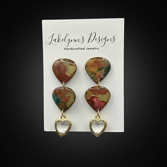 Lakelynns Designs marbled rust, gold, and green heart-shaped dangle earrings with clear faceted heart charms.