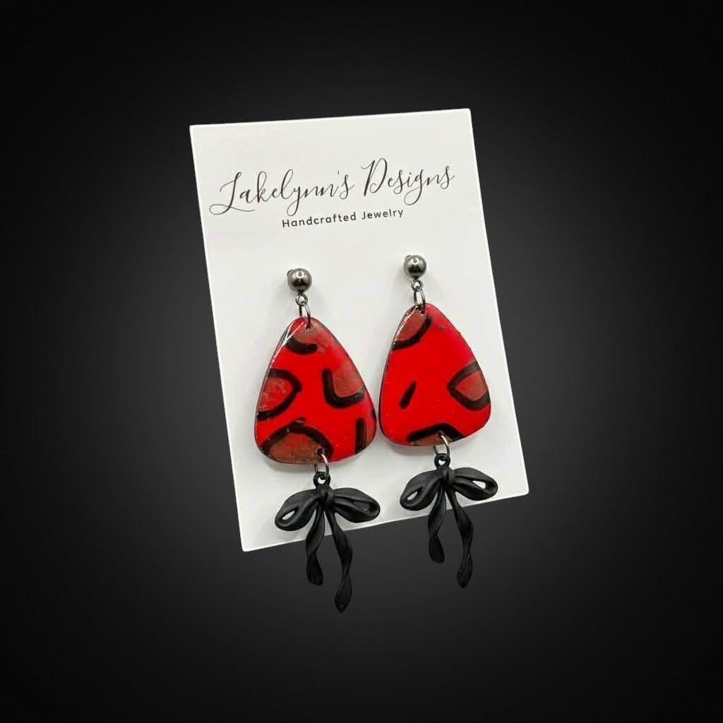 Lakelynns Designs red teardrop earrings with black abstract pattern and bow accents. Lightweight and handcrafted.