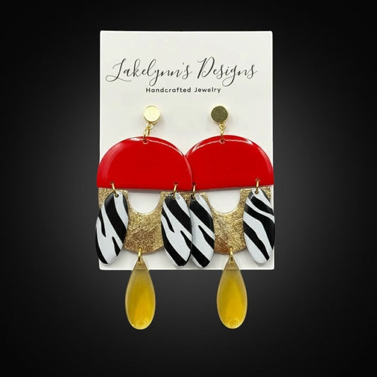 Lakelynns Designs statement earrings with red semi-circular tops, zebra print, gold accents, and yellow teardrop charms.