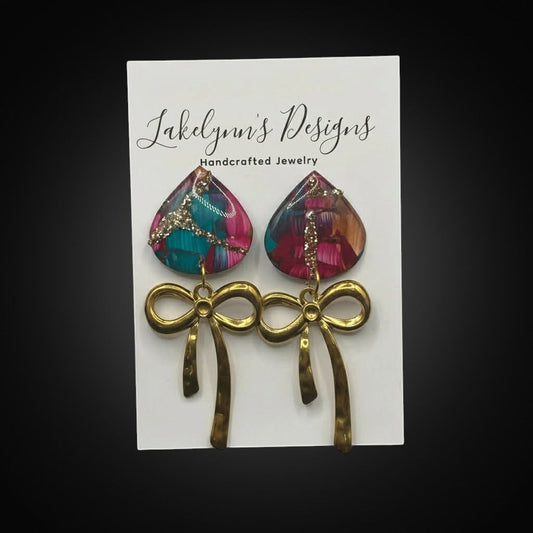 Lakelynns Designs teardrop bow earrings with abstract teal, magenta, gold pattern and glitter accents, gold-tone hammered bows.